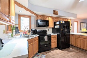 Eine moderne Küche mit Holzschränken, einem schwarzen Kühlschrank, einer Mikrowelle, einem Herd und einem Spülbecken.