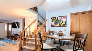 A dining area with a round table, chairs, a staircase, and a mounted TV. - Spacious A-Frame Family Beach Getaway - Sleeps 8 (Ocean Pines)