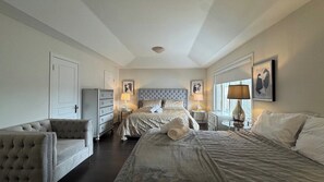 A hotel room with a large bed, a sofa, a dresser, and two bedside tables with lamps.