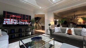 A modern living room with a flat-screen TV, a glass coffee table, a grey sofa, and a staircase leading to another level. - Richmond Hill Mansion | Ultimate Executive Retreat (Richmond Hill)