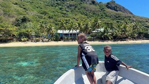 Ein Boot mit zwei Personen, klares türkisblaues Wasser, ein Strand und ein Berg im Hintergrund.