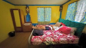 Ein Zimmer mit einem Bett, einem Holzschrank, einem Spiegel und einem Fenster mit gemusterten Vorhängen.