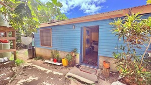 Ein kleines blaues Haus mit geöffneter Tür, einem Fenster und Blumentöpfen davor.