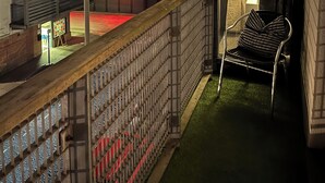 A balcony with a view of a cityscape at night, a chair, and a small table with a lamp. - Liverpool City Centre Luxury 2 Bedroom 2 Bathroom Balcony Flat - Cheap Parking (Liverpool)