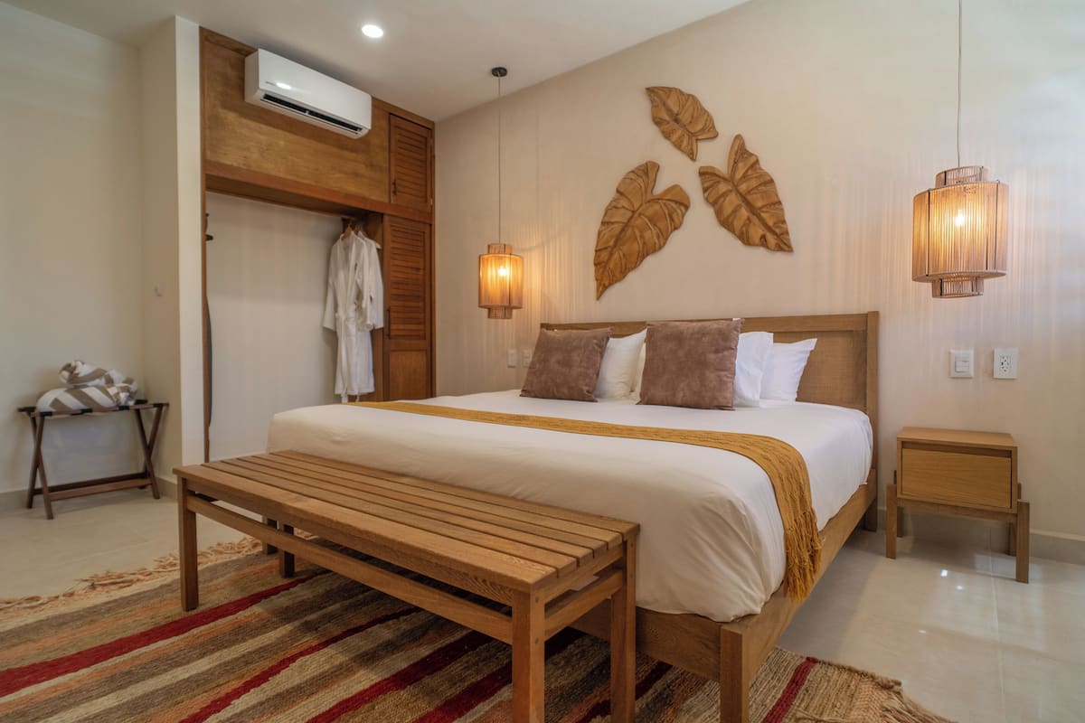 A bedroom with a bed, wooden bench, wall-mounted lights, and a small bedside table.