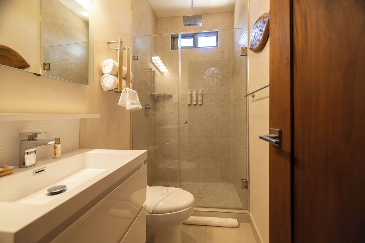 A bathroom with a glass-enclosed shower, a toilet, a sink, and a mirror.