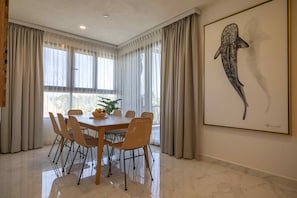 A dining area with a wooden table and wicker chairs, a large window with sheer curtains, and a framed artwork on the wall. - Hotel Kaan Holbox (Isla Holbox)