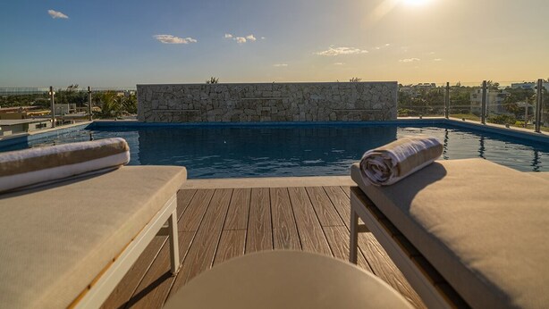 A poolside area with lounge chairs and a stone wall. - Hotel Kaan Holbox (Isla Holbox)