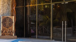 A hotel entrance with a wooden sign, glass doors, and steps leading up to the entrance. - Hotel Kaan Holbox (Isla Holbox)