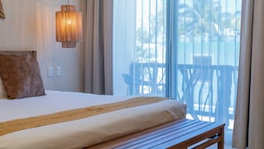 A bedroom with a bed, a wooden bench, a hanging light fixture, and a view of the outdoors through a large window. - Hotel Kaan Holbox (Isla Holbox)