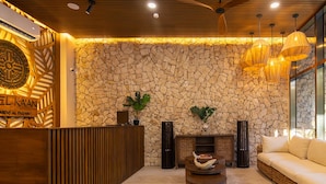 A lobby with a stone wall, wooden reception desk, round coffee table, and a sofa. - Hotel Kaan Holbox (Isla Holbox)