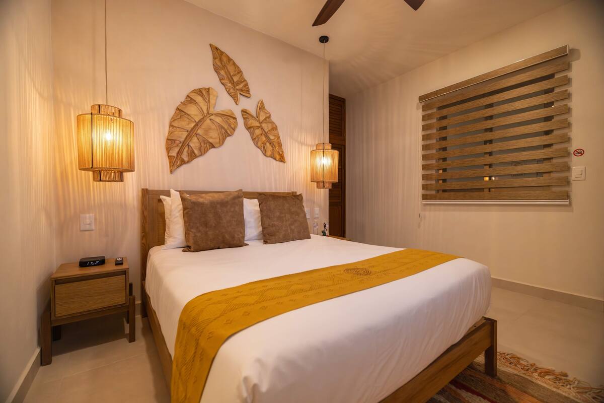 A bedroom with a bed, bedside lamps, a nightstand, a wall-mounted artwork, and a window with blinds.