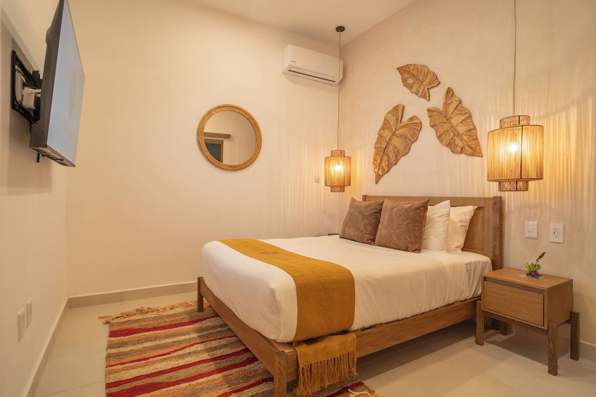 A bedroom with a bed, bedside table, wall-mounted air conditioner, and decorative wall art.