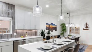 Een moderne keuken met een centraal eiland, hanglampen en een eethoek met stoelen.