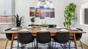 Een moderne eetkamer met een houten tafel, zwarte stoelen, een kroonluchter en wanddecoratie met woestijnmotieven.