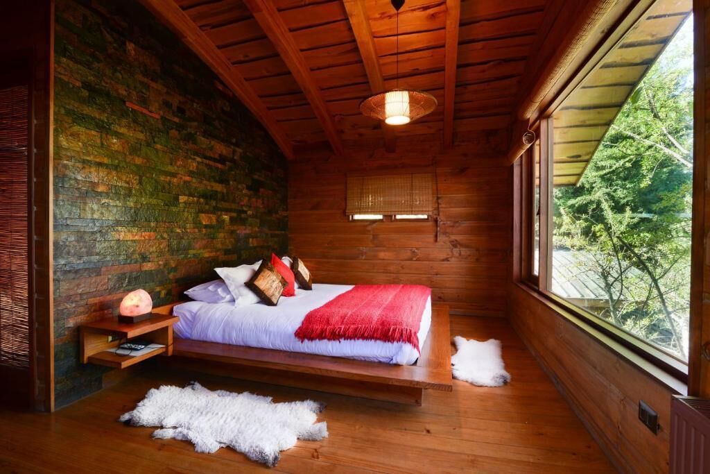A wooden cabin bedroom with a bed, a window, and a stone wall.