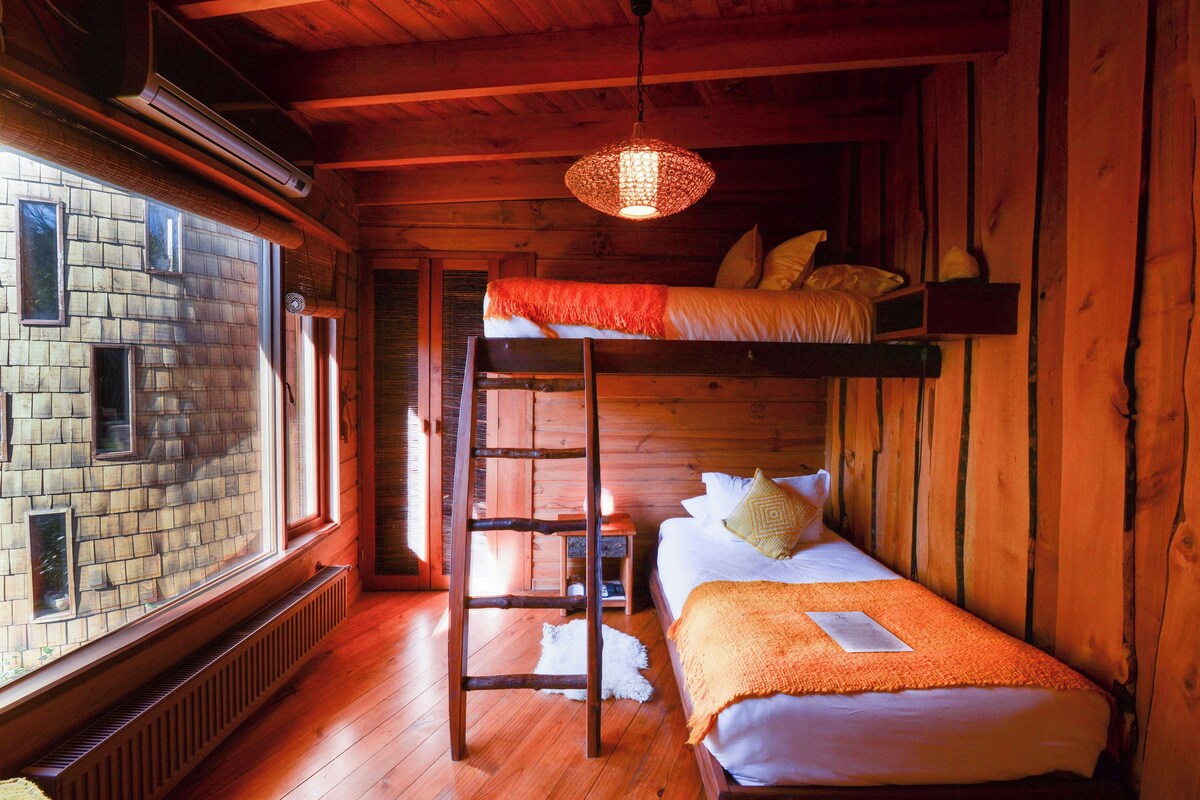 Una habitación de cabaña de madera con literas, una escalera, una ventana y una lámpara colgante.