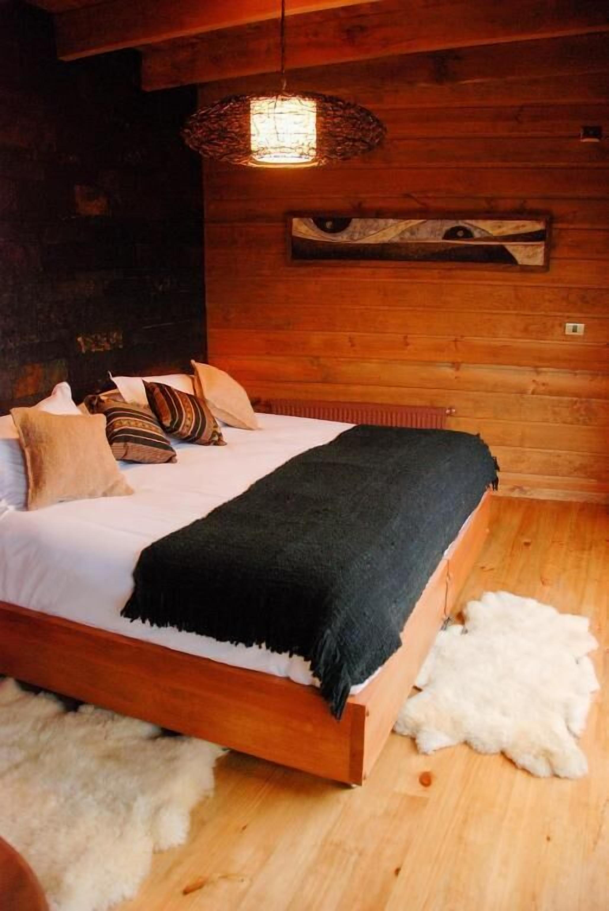 A wooden cabin interior with a bed, a woven light fixture, and a wall-mounted shelf.