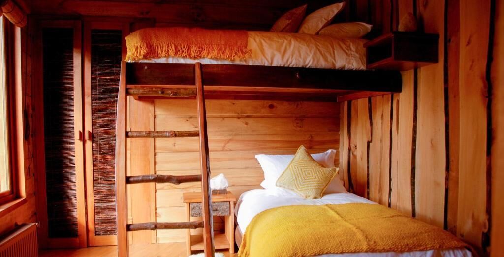 Habitación con literas de madera, una escalera y una mesita de noche con lámpara.