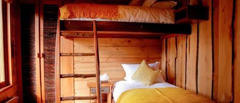 Habitación con literas de madera, una escalera y una mesita de noche con lámpara.