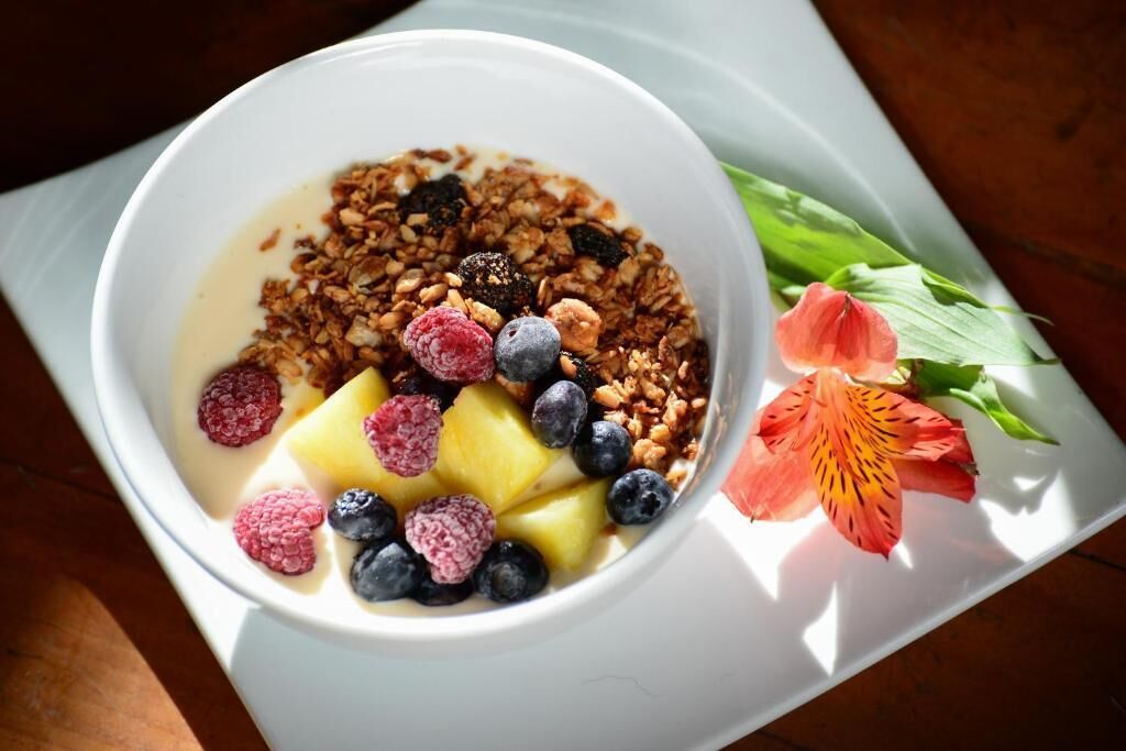A bowl of cereal with fruits and granola on a white plate.