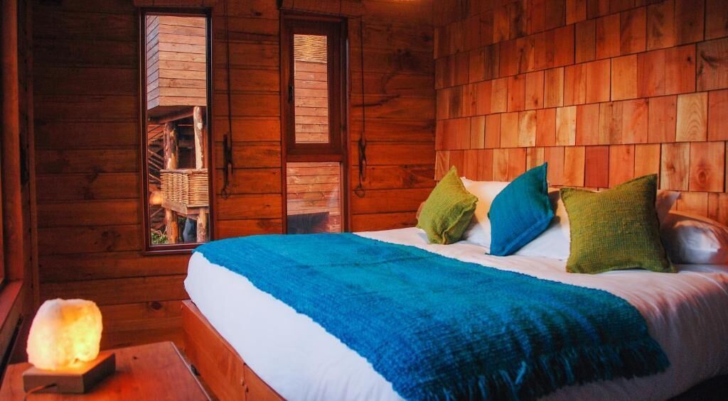 A wooden cabin room with a bed, pillows, and a salt lamp.