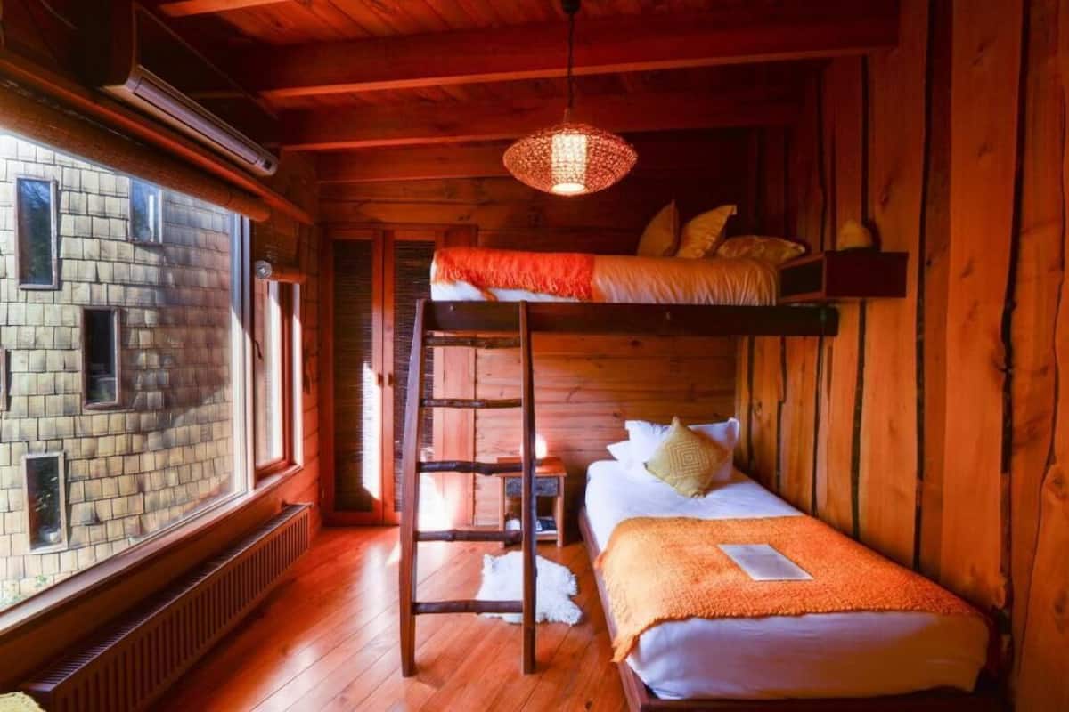 Una habitación tipo cabaña de madera con literas, una escalera, una ventana y una lámpara colgante.