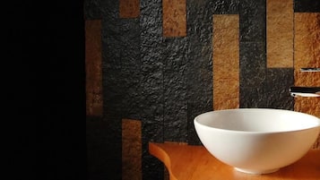 A white bowl sink with a modern faucet in a bathroom with a textured wall.