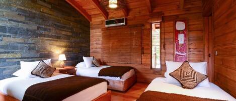 A log cabin room with two beds, a stone wall, wooden ceiling beams, and a hanging light fixture.