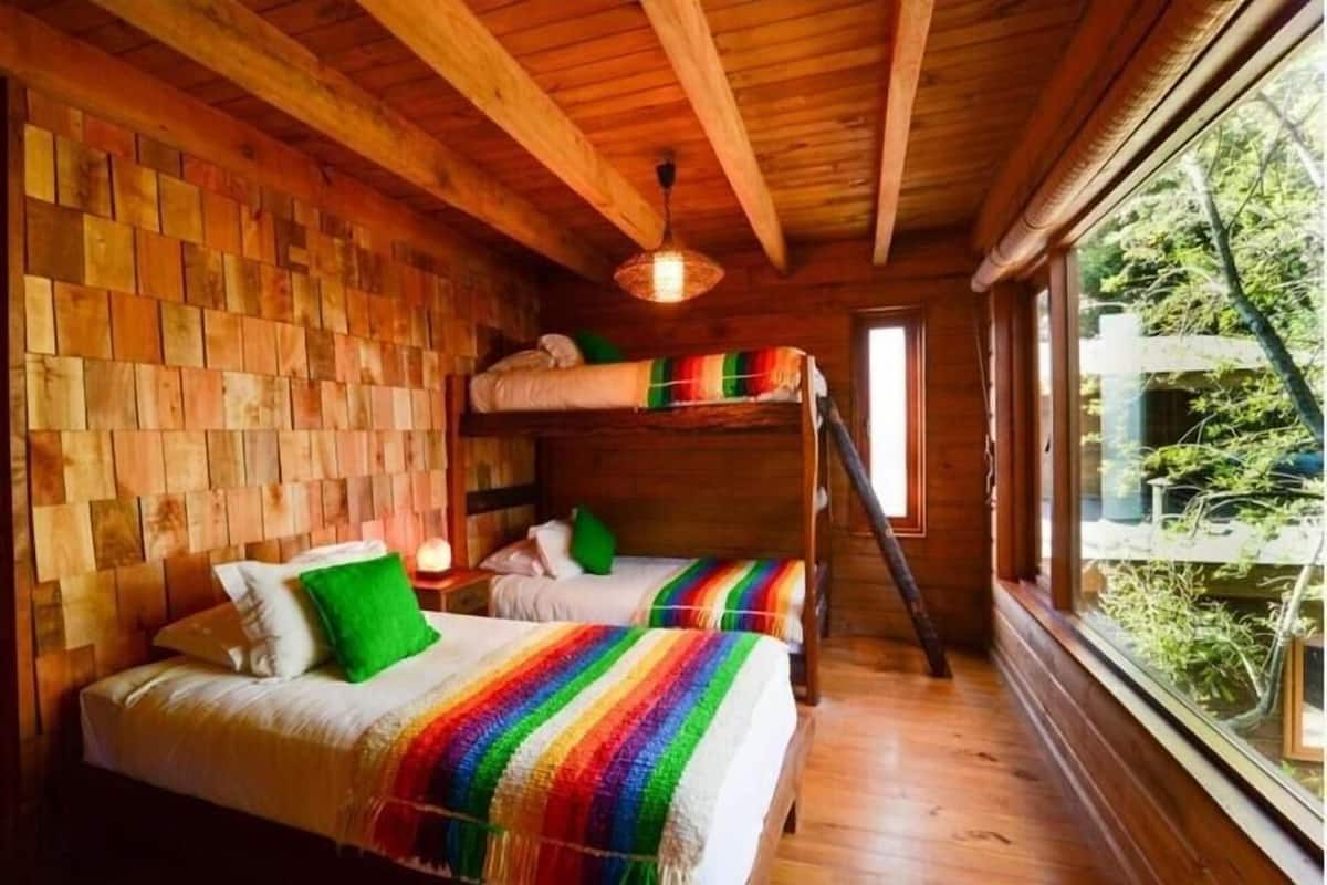 Una cabaña de madera con literas, techo de madera y ventana con vistas a la vegetación.