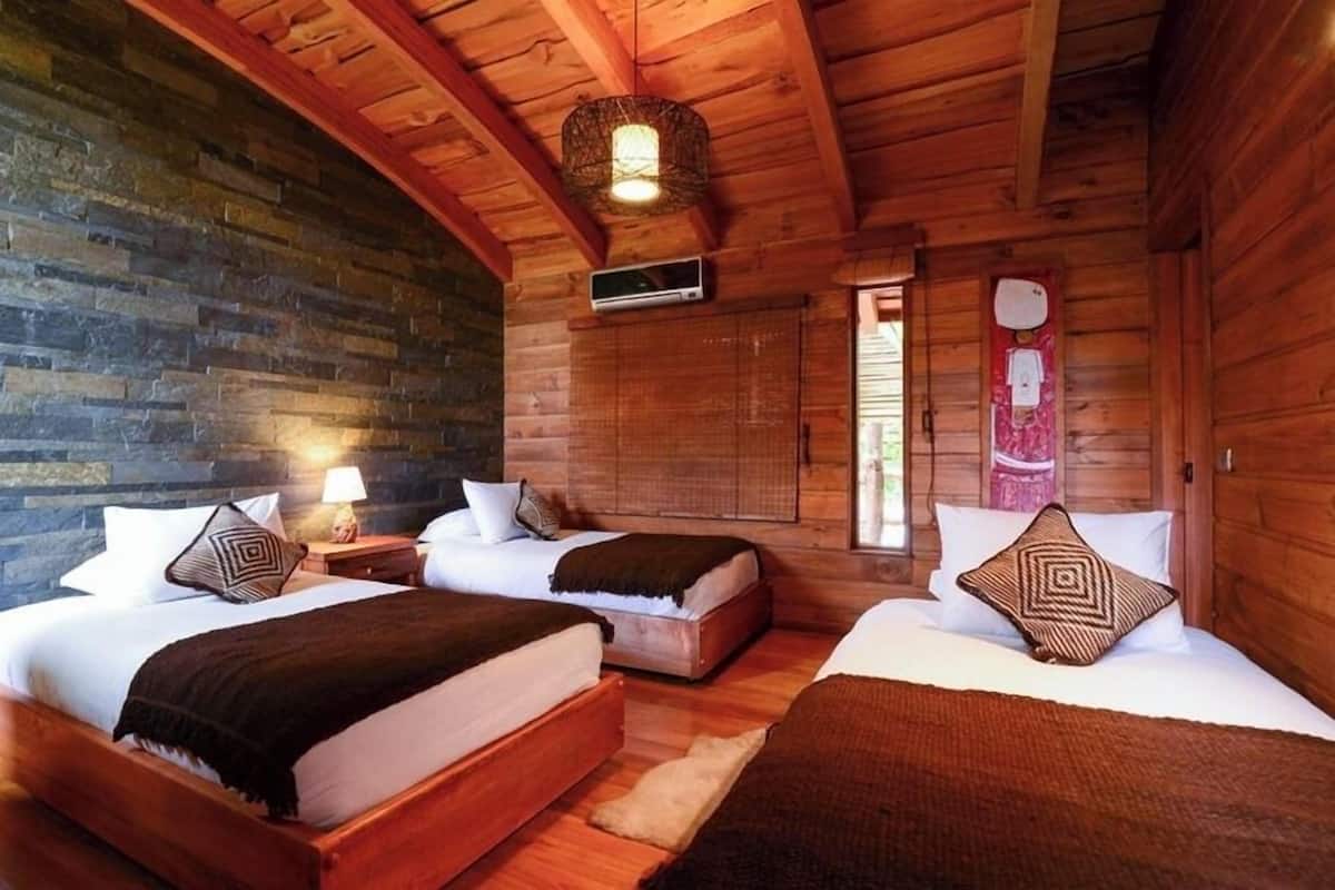 Una cabaña de madera con dos camas, una pared de piedra y una lámpara colgante.