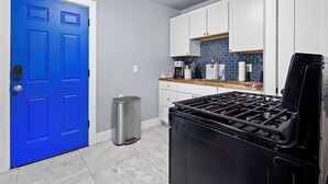 Uma cozinha com armários brancos, uma porta azul, um cesto de lixo de aço inoxidável e um fogão preto.