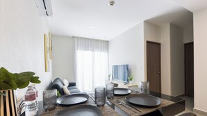 Un espace repas moderne avec une table dressée pour quatre personnes, un canapé, un téléviseur et une porte donnant sur une autre pièce.