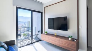 Un salon moderne doté d’un grand téléviseur, d’une porte-fenêtre coulissante donnant sur un balcon et d’une console en bois au design épuré.