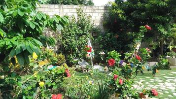 Ein Garten mit verschiedenen Pflanzen und Blumen, einer Steinmauer und einer Hängematte.