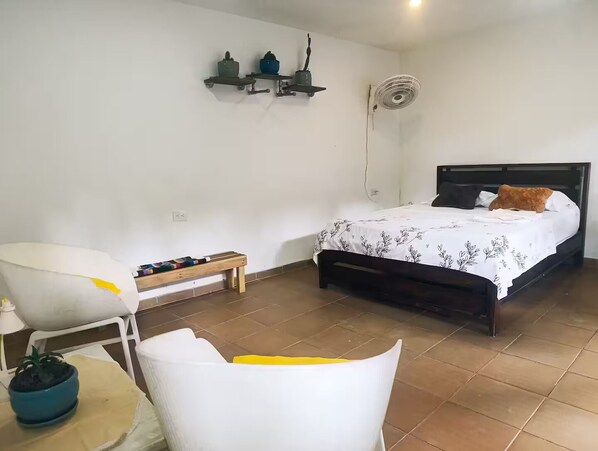 Une chambre  à coucher comprenant un lit, une chaise, une petite table et une étagère fixée au mur, ornée d’objets décoratifs.