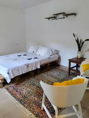 A bedroom with a bed, a small table, a chair, and a decorative plant. - Avocado: Harmony, Texture, Connection, and Peace 187715 (Palomino)