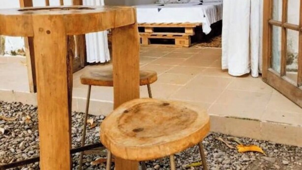 Um quarto com uma cama, uma mesa de madeira e um banquinho.