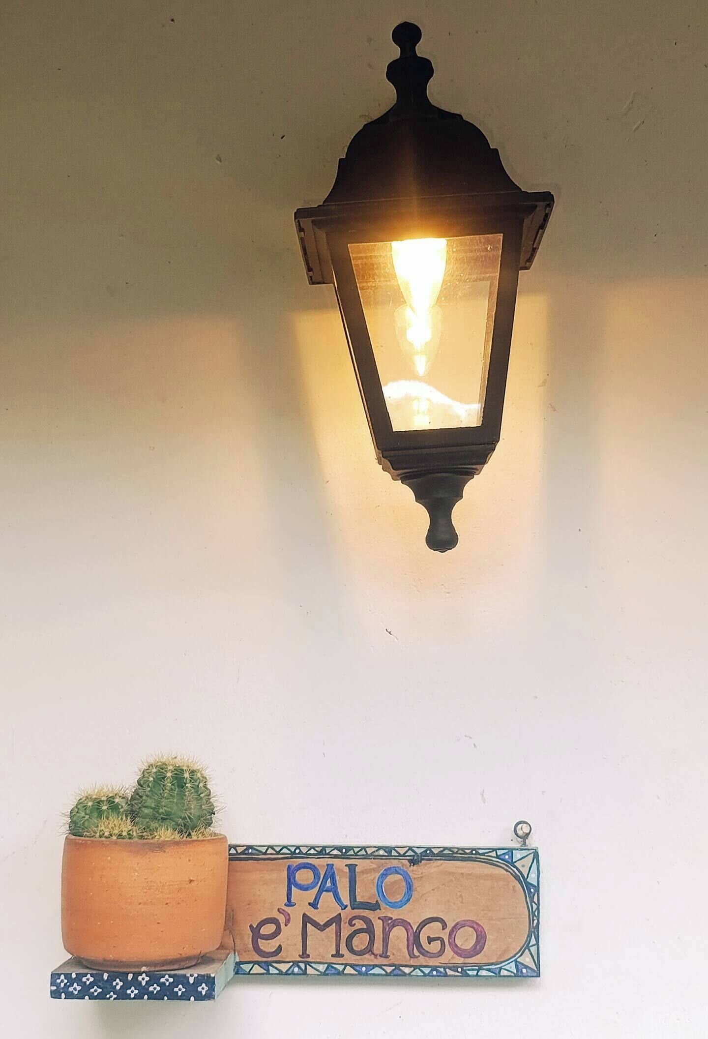 A wall-mounted lantern, a potted cactus, and a sign reading 'Palo e Mango'.