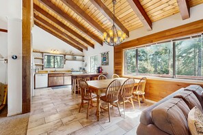 Eine geräumige Küche mit Holzbalken, ein Essbereich mit Holzkästen und ein großes Fenster mit Blick auf einen Wald.