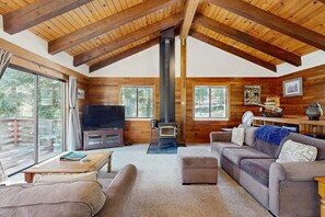 Ein gemütliches Blockhausschlafzimmer mit Holzbalkendecke, Kamin, Fernseher und einer Couch.