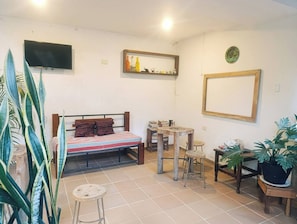 A small, tidy room with a bed, a TV, a mirror, and a few stools.