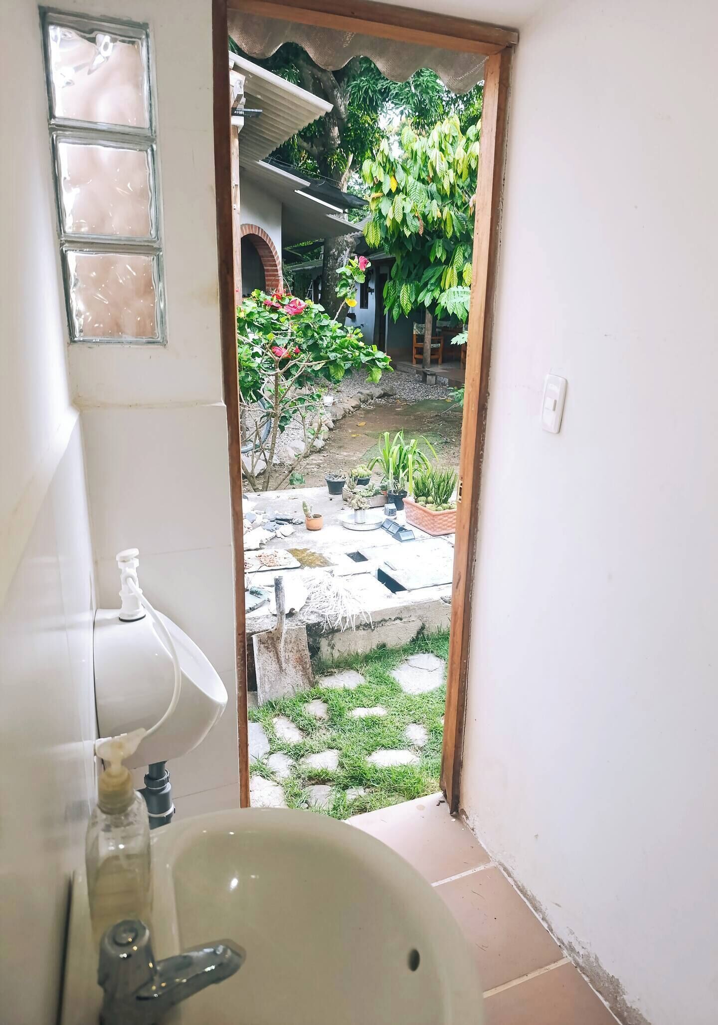 Une salle de bain avec un lavabo, un miroir et une vue sur un jardin, accessible par une porte ouverte.