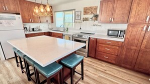 Una cocina con armarios de madera, una isla grande con taburetes, electrodomésticos de acero inoxidable e iluminación colgante.