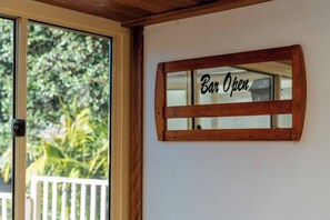 Un letrero de madera con la inscripción 'Bar Open', colocado en una pared junto a una puerta corredera de vidrio que ofrece vista a la vegetación exterior.