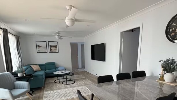 Una sala de estar moderna con un sofá, una mesa de comedor con sillas, un ventilador de techo y un televisor montado en la pared.
