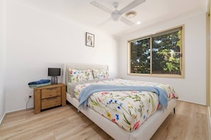 A bedroom with a bed, a nightstand, a ceiling fan, a window with a view of trees, and a wall-mounted picture. - The Sunroom Guesthouse by Esteem Retreats (Stanhope Gardens)