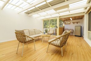Um quarto com piso de madeira, um sofá, duas cadeiras, uma mesinha e uma geladeira.