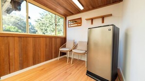 Una habitación con piso de madera, un refrigerador empotrado y dos sillas de mimbre.