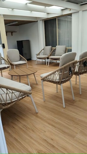 Une pièce avec des chaises en osier, une petite table et une grande fenêtre avec des rideaux.